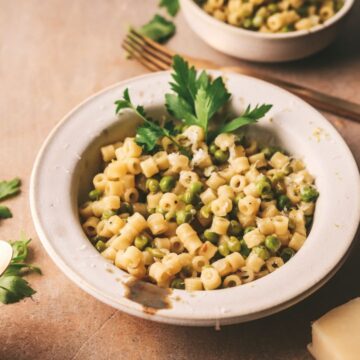 Pasta e piselli with parsley and cheese, plus utensils.