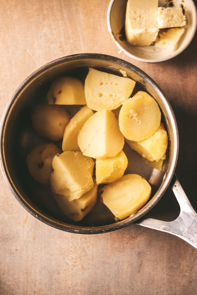 The potatoes, boiled, in a pot, drained.