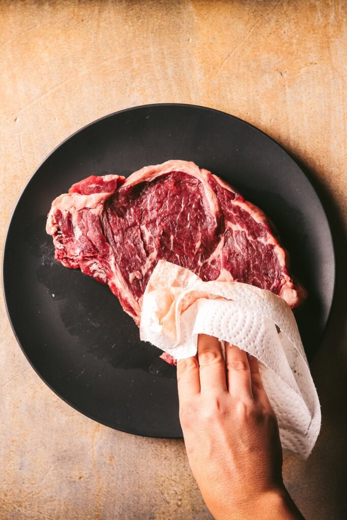 Patting the steak dry with a paper towel. 