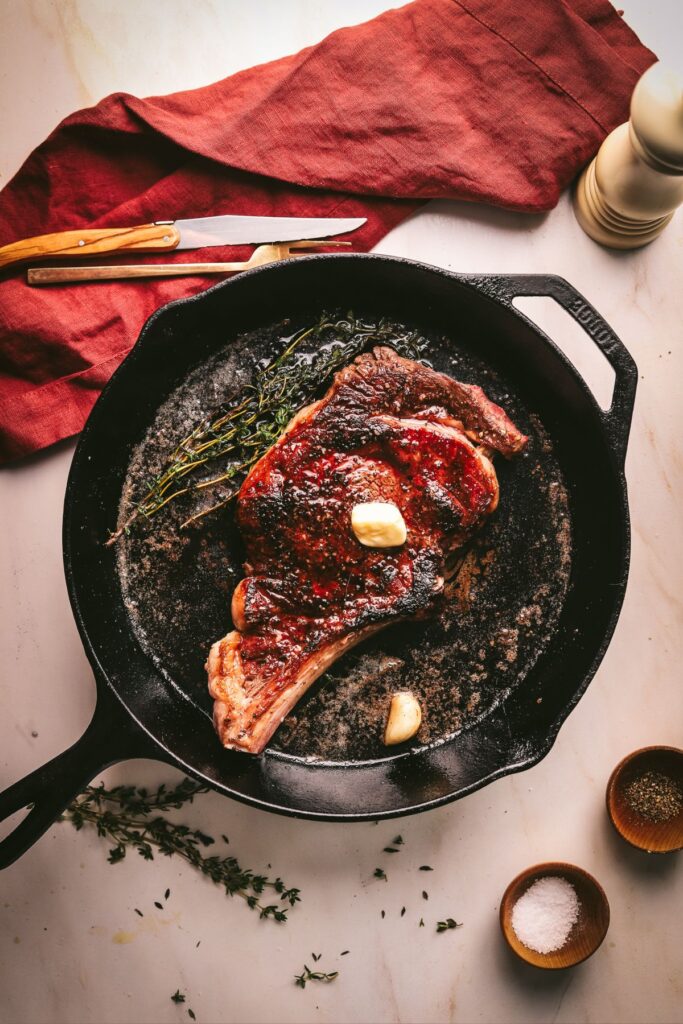 A bone-in ribeye steak in a cast iron skillet with butter and herbs. 