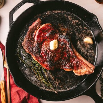 Seared ribeye steak in a cast iron with napkin and cutlery.