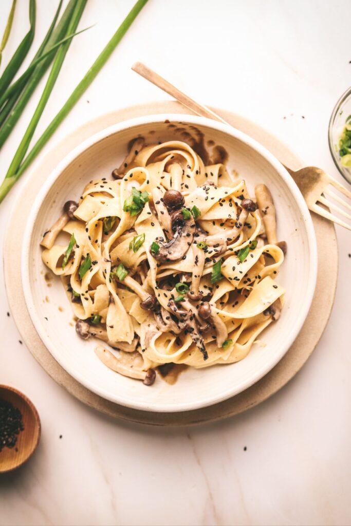 A bowl of Miso mushroom pasta with green onion and sesame seeds.
