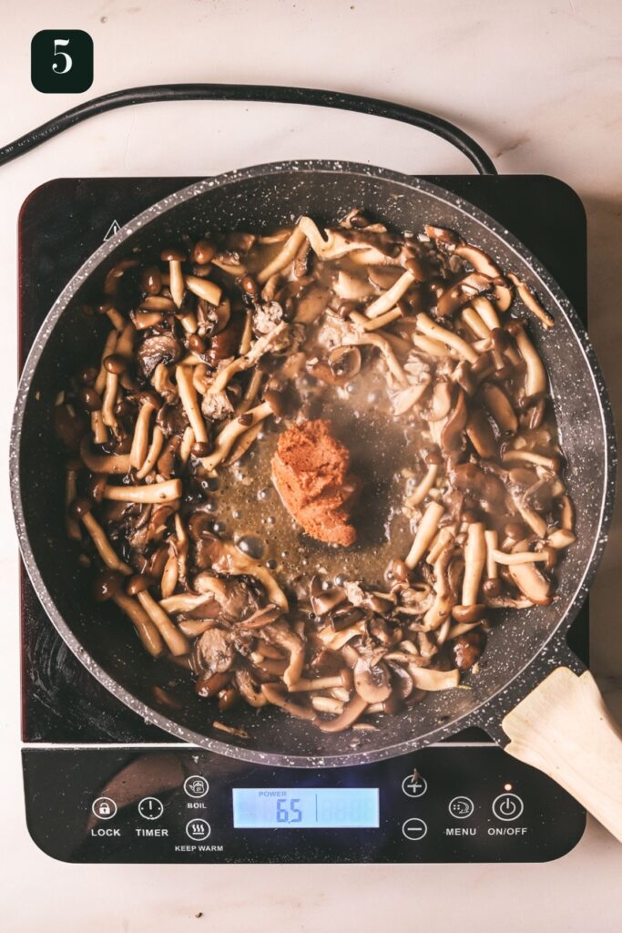Adding miso to the pan with the mushrooms. 