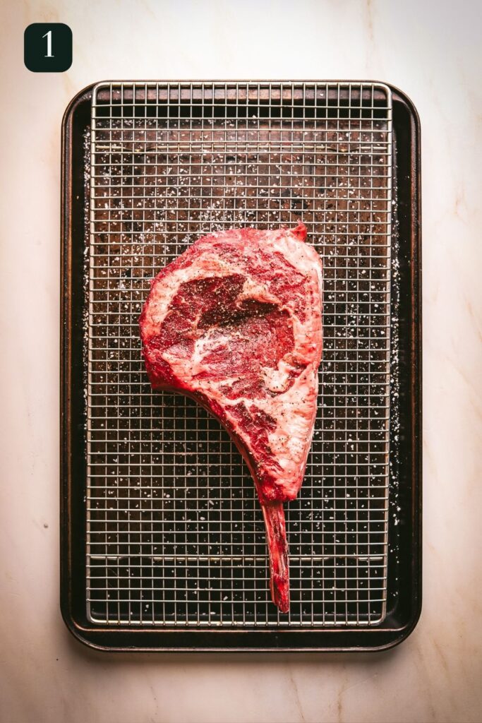Raw tomahawk steak, on a cooling rack that's nestled inside a baking sheet. 