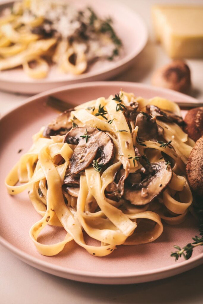 A pile of creamy mushroom pasta with white wine sauce on a plate with parmesan cheese. 