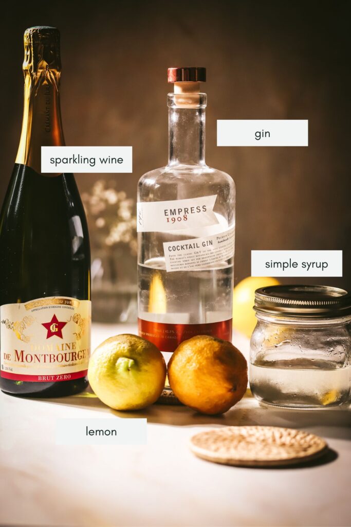 The ingredients for a French 75 cocktail, labelled, sparkling wine, gin, lemon, simple syrup.