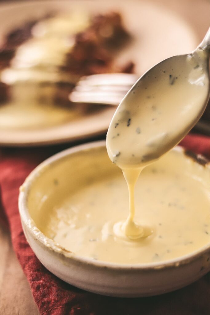 A spoonful of béarnaise sauce in a bowl, steak in the background. 