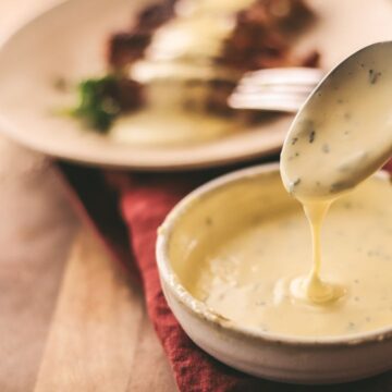 Béarnaise sauce in a bowl dripping off a spoon.