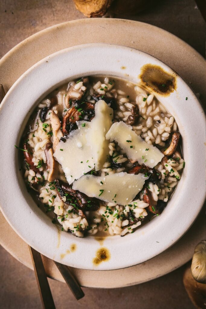 A bowl of mushrooms risotto, with parmesan shards, chives and served on a table. 