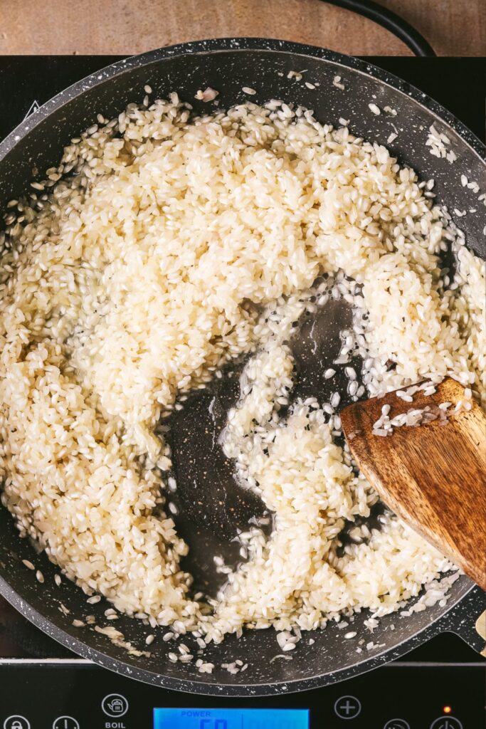 Adding the white wine to the rice and shallots, stirring. 