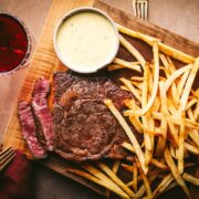 A platter of steak, fries and béarnaise sauce along with red wine.