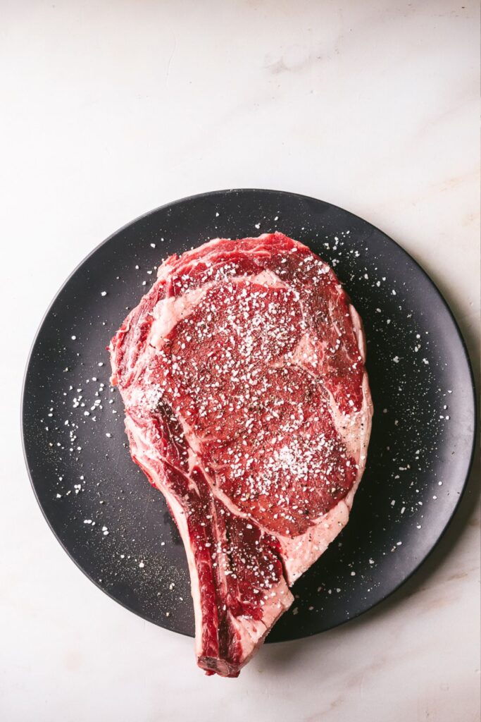 A large, bone-in ribeye steak seasonsed with salt and pepper. 