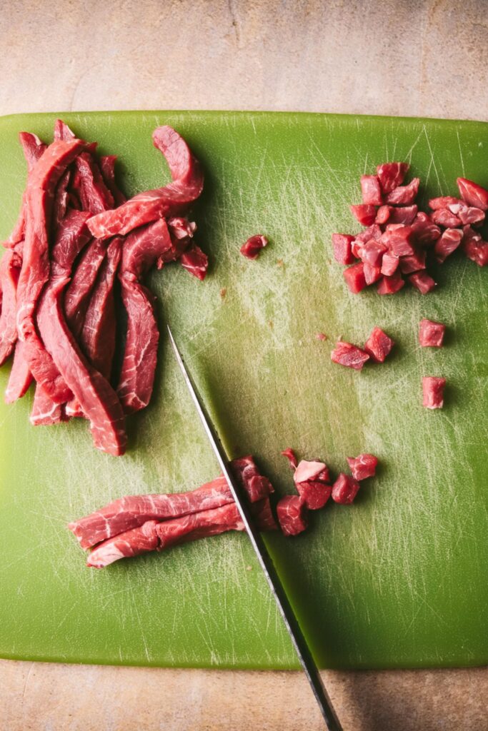 Steak is in thin strips, now being cut into small cubes. 