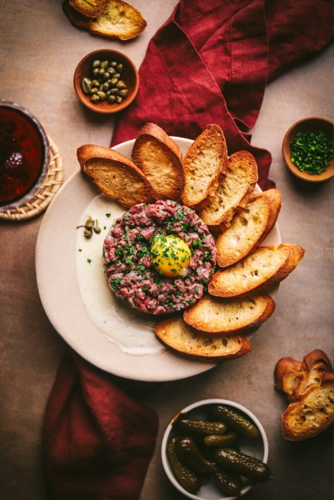 Steak tartare with aioli, egg yolk, and baguettes with napkins and garnishes. 