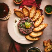 Beef tartare with baguettes, herbs, wine, and napkins.