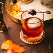 A maple old fashioned, garnished with a cocktail pick and a cherry.